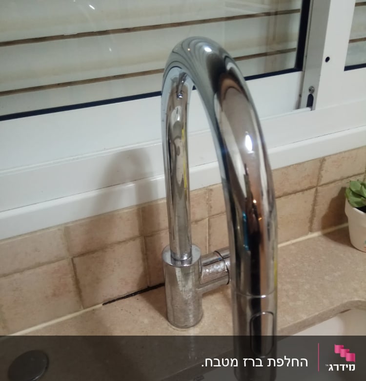 ברז מטבח כסוף על משטח שיש ליד חלון